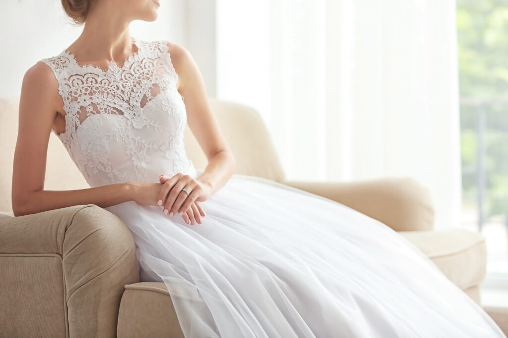 Bride in beautiful wedding gown sitting on sofa