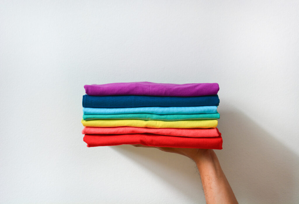 close up stack of folded multicolored t-shirt in hand